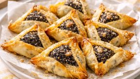 אוזני המן טבעוניות מבצק פילו במילוי פרג עשיר, מוגשות על צלחת עם אגוזי מלך ודבש לצד נענע טרייה