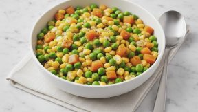 תוספת ירקות חמה של אפונה, תירס וקוביות גזר מבושלים בקערה לבנה עם כף לצד מפית בד